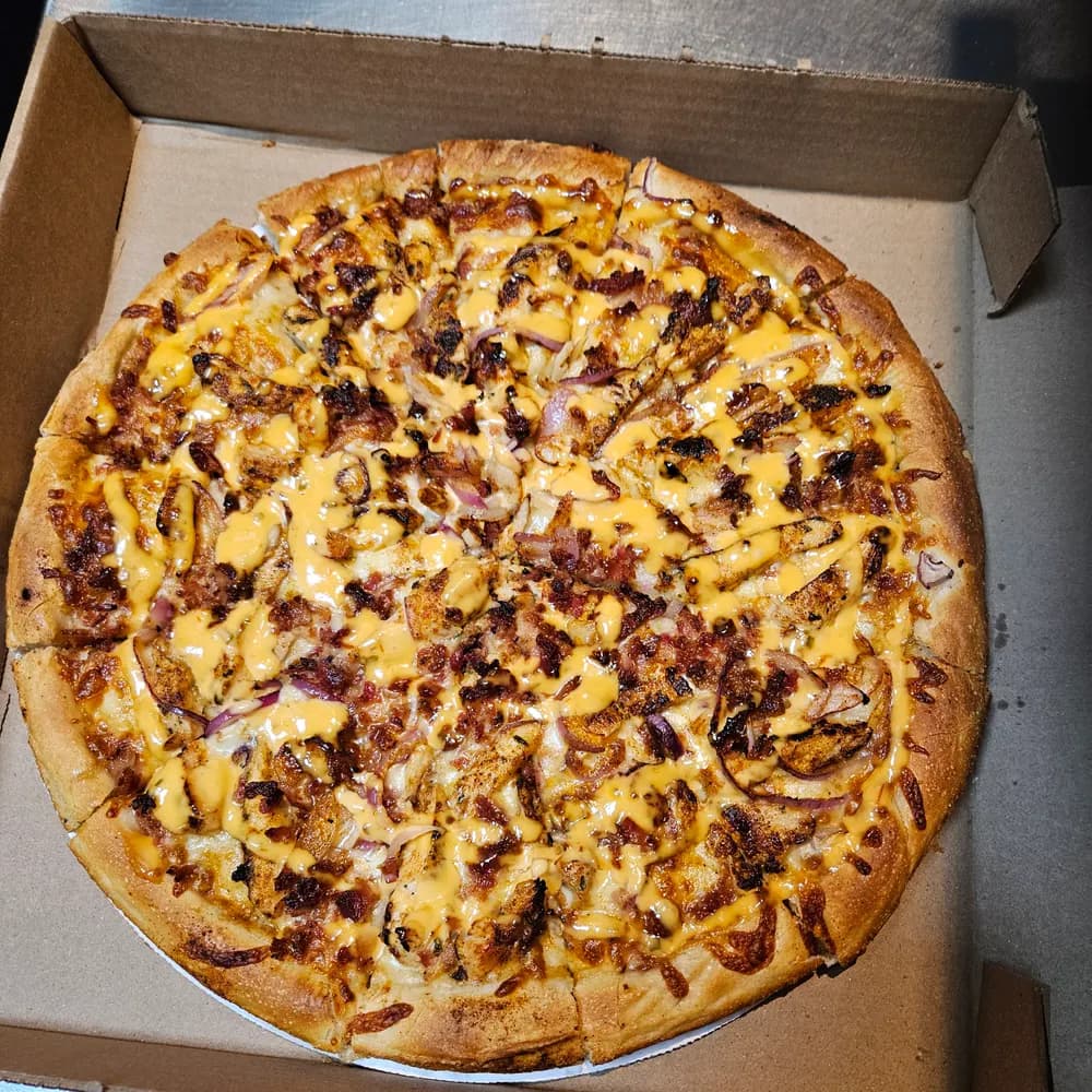 Pizza topped with grilled chicken, bacon, red onion and a cheese-sauce drizzle